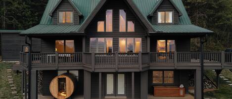 A two-story log cabin with a balcony, a large wooden barrel, and a stone staircase.