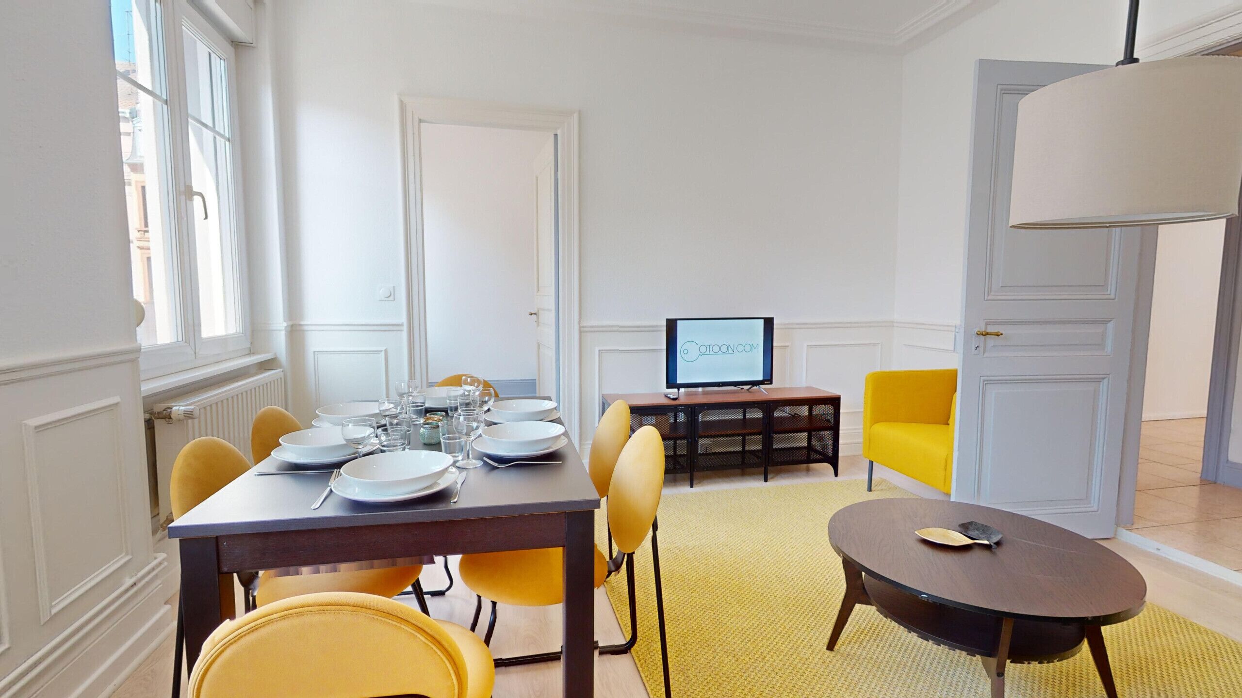 A dining area with a table set for four, a television on a stand, and a yellow armchair.