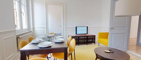 A dining area with a table set for four, a television on a stand, and a yellow armchair.