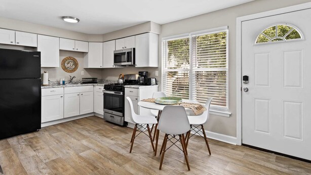 Una cocina moderna con armarios blancos, un refrigerador negro y una zona de comedor con mesa y sillas.