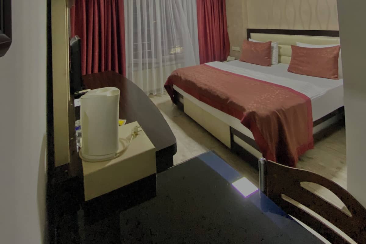 Ein Hotelzimmer mit Bett, Schreibtisch, Stuhl, Klimaanlage und einem Vorhangfenster.