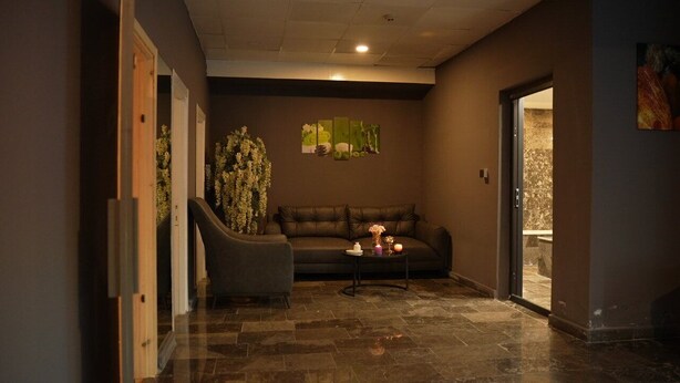 A hallway with a dark brown wall, a leather sofa, a small table with candles, and a staircase with white flowers. - Sivas Azze Palace Otel (Sivas)