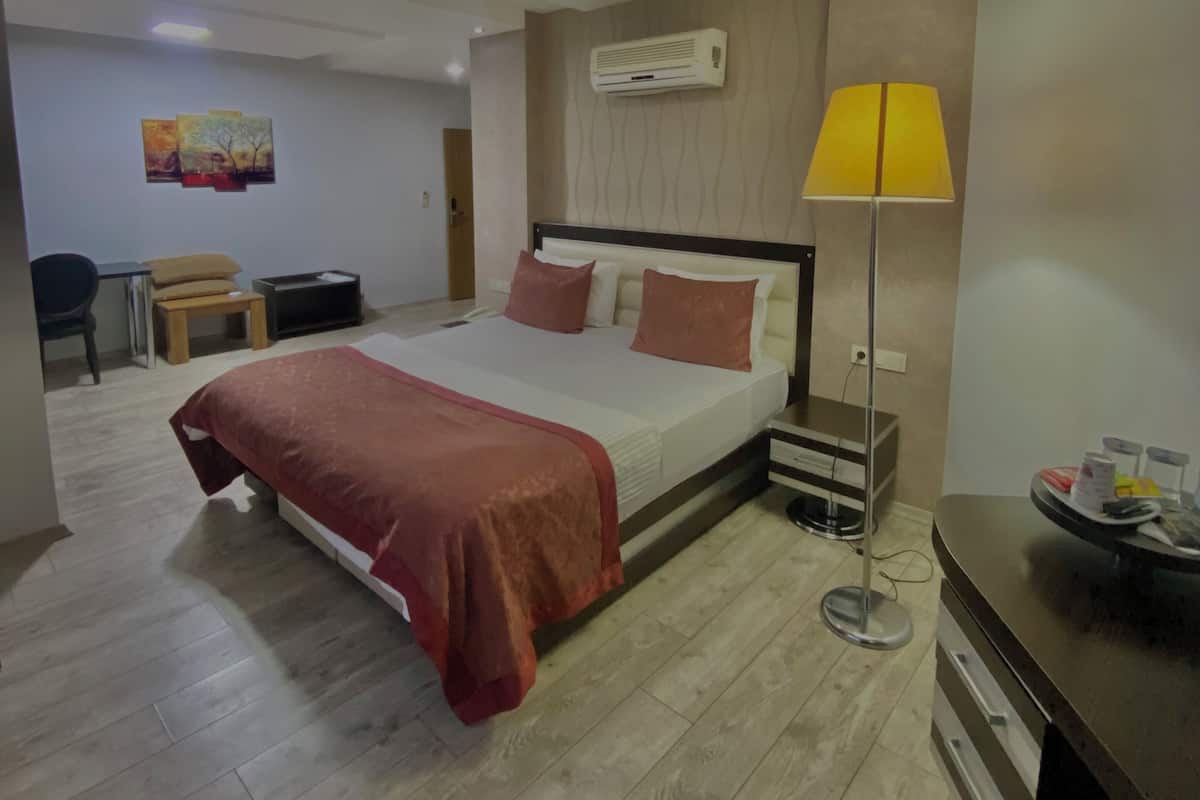 Ein modernes Hotelzimmer mit Bett, Nachttisch, Lampe und Schreibtisch mit Stuhl.
