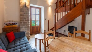 Un salón acogedor con pared de piedra, escalera de madera, sofá, mesa de comedor y televisor.