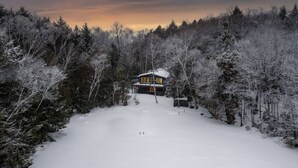 A snow-covered landscape with a house surrounded by trees. - Serene, breathtaking waterfront views in Muskoka, half an hour from Algonquin! (Huntsville)