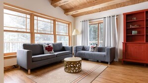 A cozy living room with two grey sofas, a wooden coffee table, and a red bookshelf. - Serene, breathtaking waterfront views in Muskoka, half an hour from Algonquin! (Huntsville)
