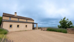 Una casa de dos pisos con un camino de tierra y un muro de piedra.