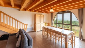 Un amplio espacio habitable con una escalera de madera, una mesa de comedor con sillas y un ventanal con vistas al exterior.