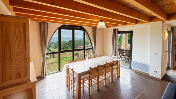 Una habitación amplia con una gran mesa de comedor, vigas de madera en el techo y vistas al exterior.