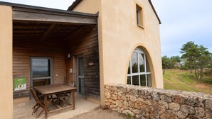 Un edificio rústico con una mesa y sillas de madera afuera, un muro de piedra y una ventana con arco.