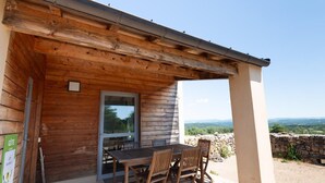 A wooden cabin with a table and chairs outside, a window, and a view of the landscape. - La Baumelle 4/6 persons (SAINT-PIERRE-DES-TRIPIERS)
