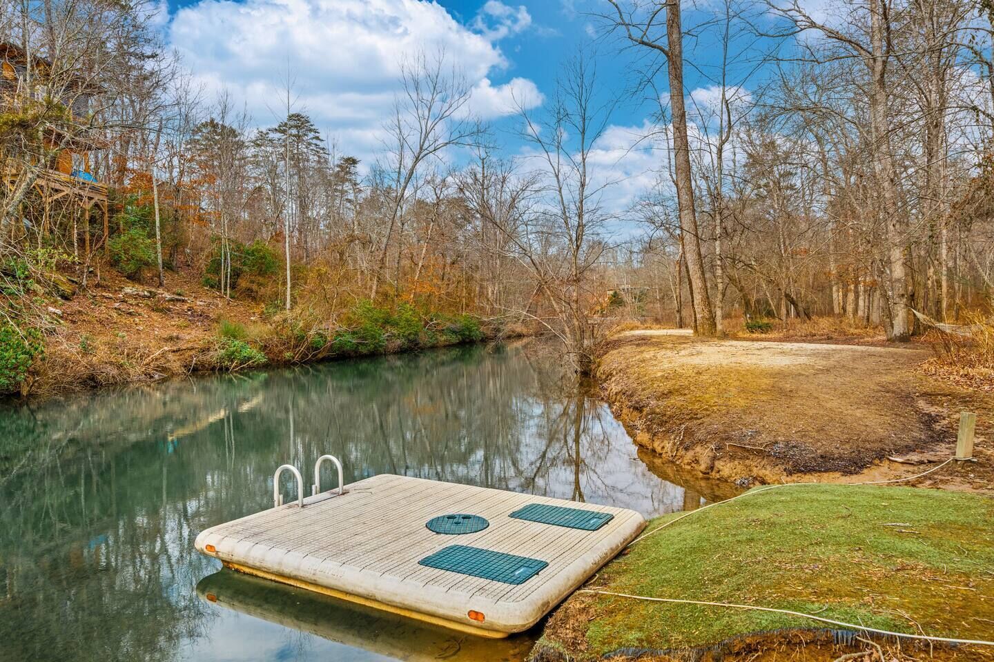 A wooden dock extending into a calm river, surrounded by trees and a grassy area.