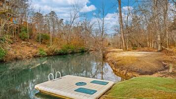 A wooden dock extending into a calm river, surrounded by trees and a grassy area.
