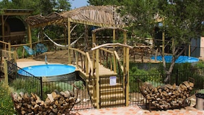 Ein Poolbereich mit Holzterrasse, Schwimmbecken und überdachter Sitzgelegenheit.