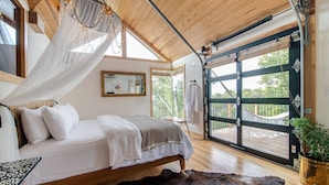 Ein Schlafzimmer mit einem Bett, einem großen Fenster, einer Hängematte und Blick ins Freie.
