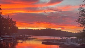 Ein Sonnenuntergang über einem ruhigen See mit angestaubten Booten, einem sandigen Ufer und einer Person mit einem Hund.