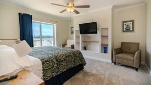 A bedroom with a bed, a chair, a TV mounted on the wall, and a ceiling fan. - Intracoastal Retreat (Hubert)