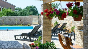 A poolside area with lounge chairs, a stone wall, and hanging flower baskets. - Beautiful home in Vodnjan (Vodnjan)