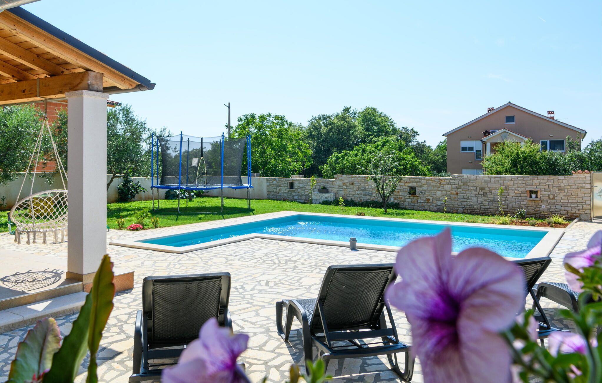 A backyard with a swimming pool, a trampoline, and outdoor seating.