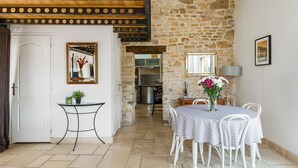A dining area with a stone wall, a white door, a small table with a glass top, and a round table with white chairs.