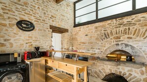 A rustic stone kitchen with a stone oven, a washing machine, and a wooden table.