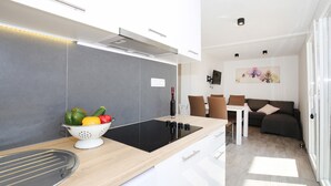 A modern kitchen with a black induction cooktop, a colander with vegetables, and a wine bottle. - Beautiful home in Murter (Murter)