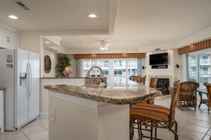 A kitchen with a central island, a refrigerator, a dining area with wicker chairs, and a fireplace.