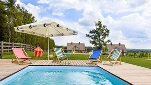 A swimming pool with four lounge chairs and a large umbrella.