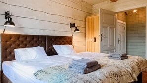 A bedroom with a tufted headboard, two bedside lamps, a bed with white linens, a patterned throw blanket, and a wooden wardrobe with a door.