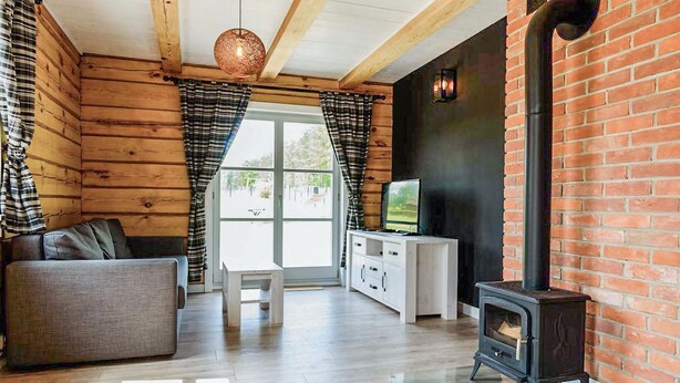 A cozy living room with wooden walls, a sofa, a TV on a white cabinet, and a wood-burning stove.