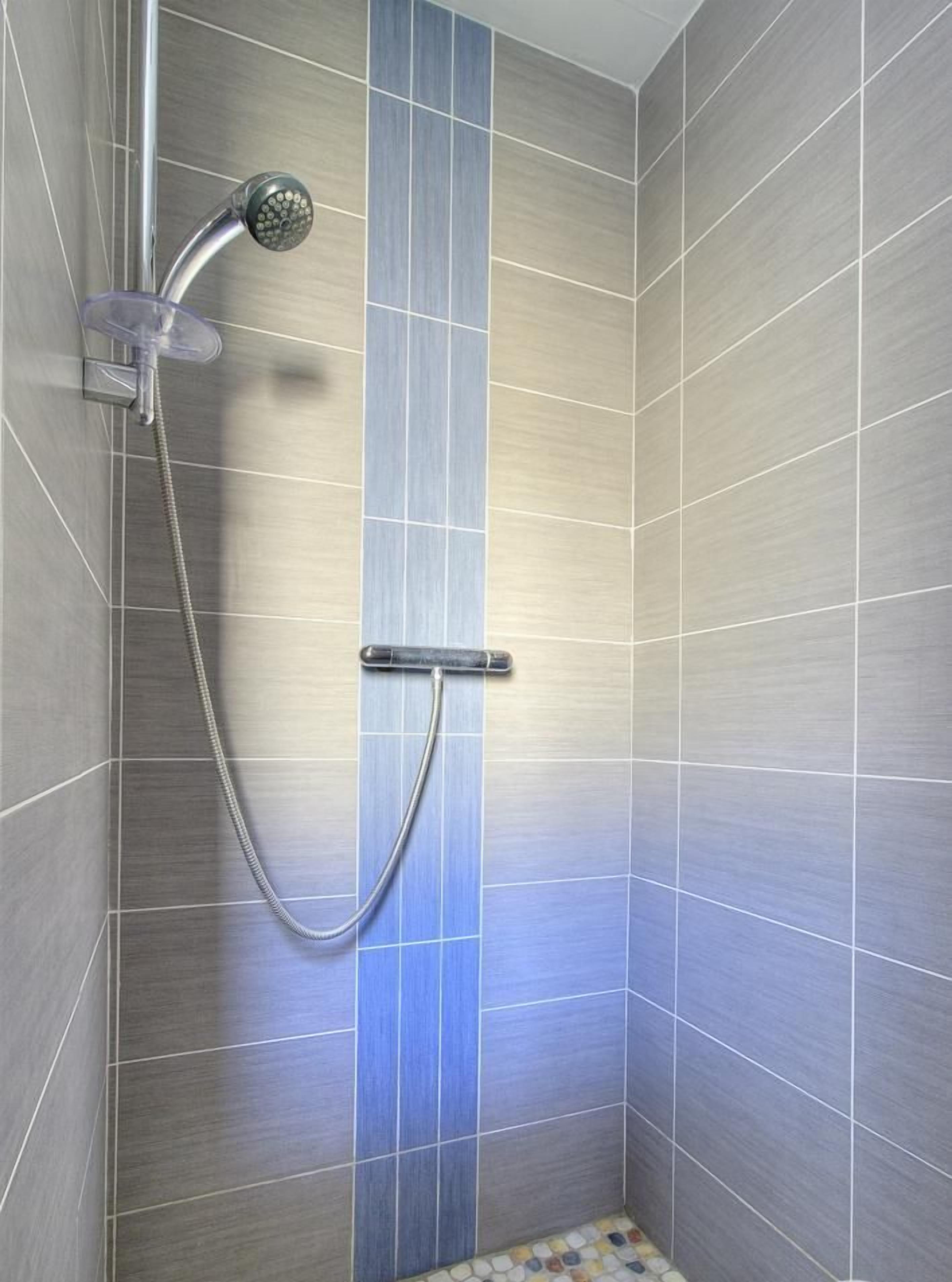 Een douche met een handdouche en een bediening aan de muur.