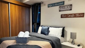 A neatly made bed with a dark blue and beige duvet, a bedside table with a lamp, and motivational wall art. - Apartment W/Balcony overlooking downtown (Guatemala city)