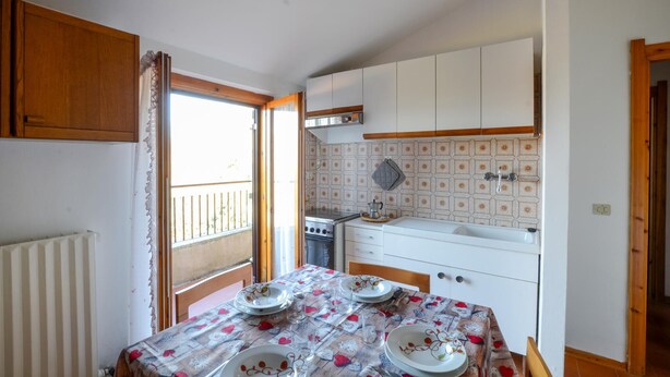 A compact kitchen with white cabinets, a stove, and a sink. There's a dining table with a floral tablecloth and plates. - Pet friendly apartment in Tavarone (Tavarone)