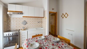 A compact kitchen with white cabinets, a stove, and a dining area with a table set for four. - Pet friendly apartment in Tavarone (Tavarone)