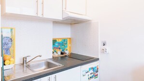 A kitchen with white cabinets, a stainless steel sink, and a black countertop. - Stylish Studio 12 Min from Republique (Paris)