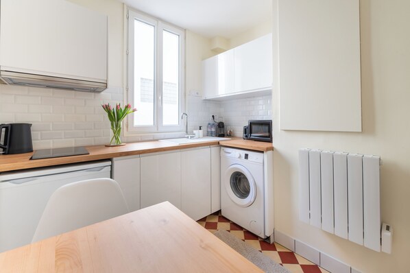 A modern kitchen with white cabinets, a washing machine, a microwave, and a window.