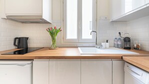 Eine moderne Küche mit weißen Schränken, einer Holzarbeitsplatte, einem schwarzen Wasserkocher, einer Vase mit Blumen und einem Fenster über der Spüle.