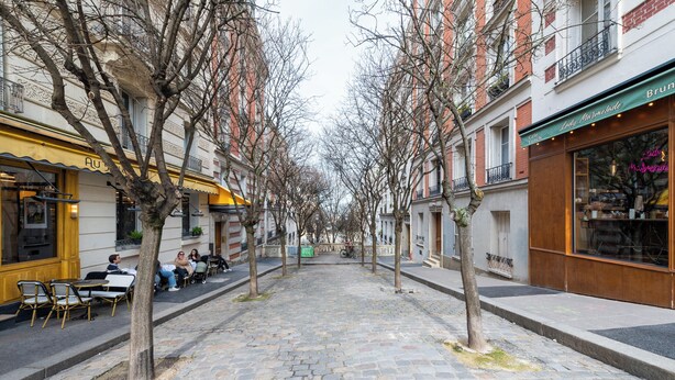 Eine Kopfsteinpflasterstraße gesäumt von Bäumen und Gebäuden, darunter ein Café und ein Restaurant.