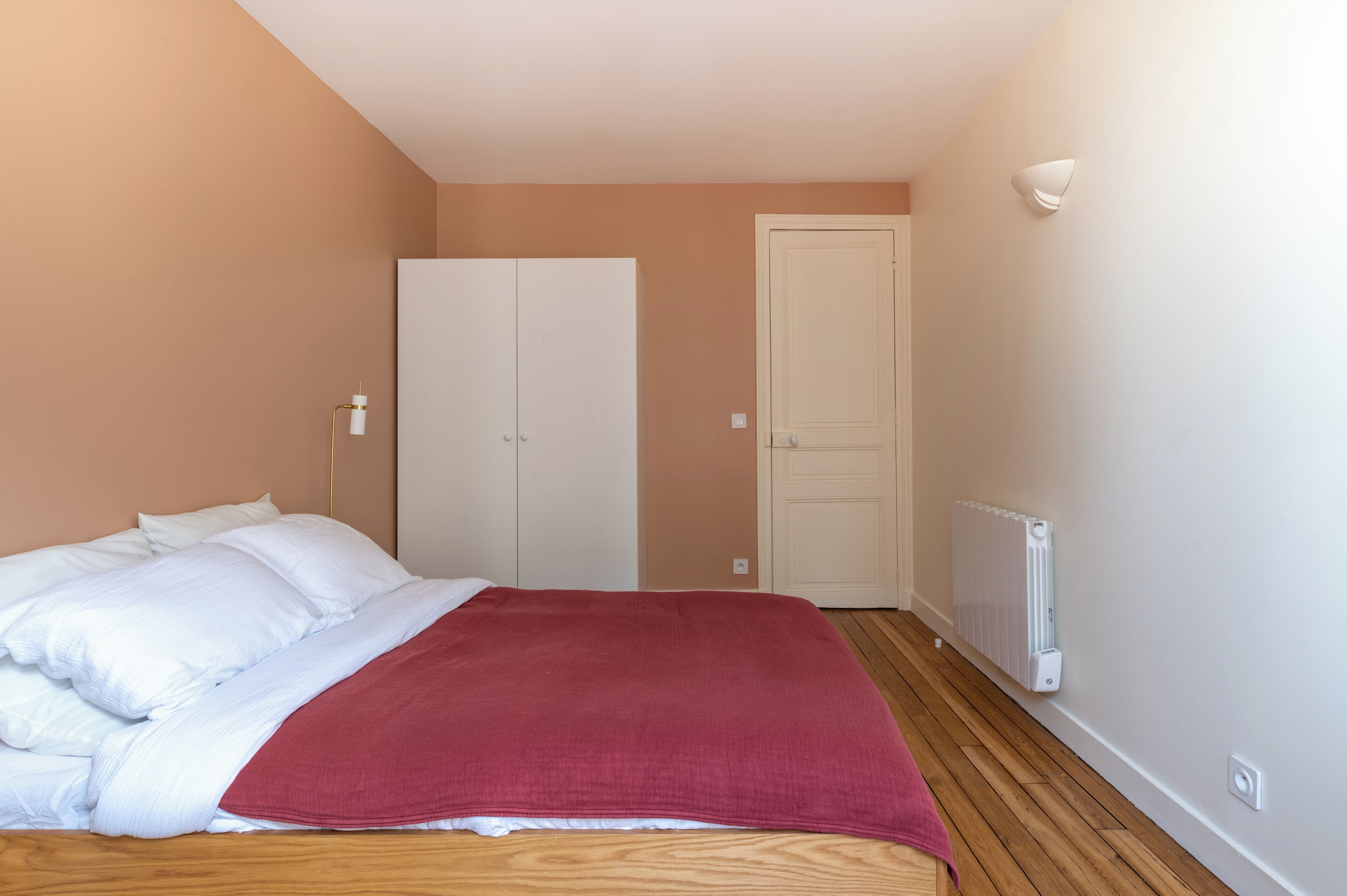 Een slaapkamer met een bed, een kast, een radiator en een deur.