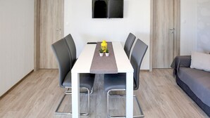 A modern room with a dining table, four chairs, a flat-screen TV mounted on the wall, and a sofa.