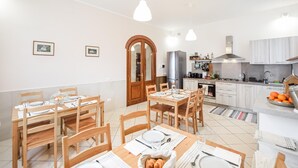 Una cocina moderna con armarios blancos, un refrigerador de acero inoxidable y un comedor con mesas y sillas de madera.