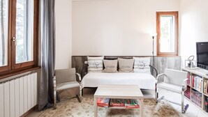Una habitación acogedora con una cama, una mesita, una estantería y un ventanal con cortinas.