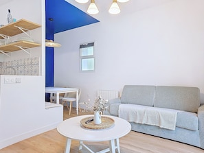 A modern living room with a grey sofa, a white round table with a vase, a dining area with a white table and chairs, and a blue accent wall. - Appartement Le Porto, Cosy et Chaleureux ! (Cholet)