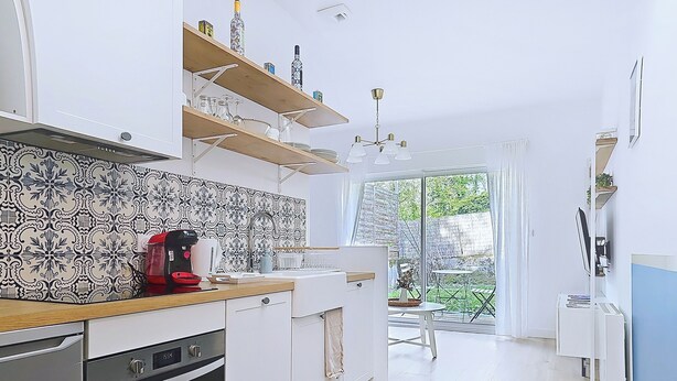 A modern kitchen with a built-in oven, a coffee maker, and a dining area with a table and chairs. - Appartement Le Porto, Cosy et Chaleureux ! (Cholet)