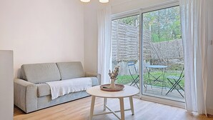 A room with a sofa, a small table with a vase, and a large sliding glass door leading to an outdoor area. - Appartement Le Porto, Cosy et Chaleureux ! (Cholet)
