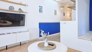 A modern living room with a TV, white furniture, a blue accent wall, and a ceiling light fixture. - Appartement Le Porto, Cosy et Chaleureux ! (Cholet)