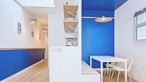 A modern room with a white bench, a small table, and a blue accent wall. - Appartement Le Porto, Cosy et Chaleureux ! (Cholet)