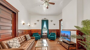 A spacious living room with a leather sofa, teal armchairs, a glass coffee table, and a television. - The Victorian on South Park • Sleeps 6 (Buffalo)