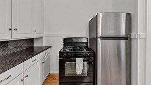 A kitchen with white cabinets, a black stove, and a stainless steel refrigerator. - The Victorian on South Park • Sleeps 6 (Buffalo)