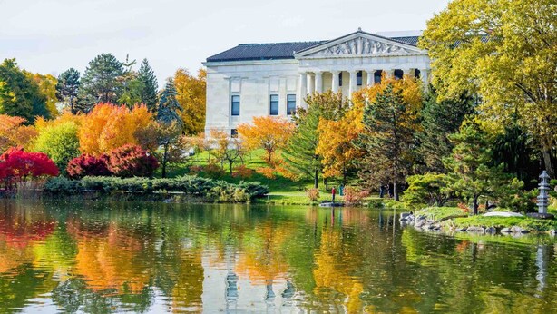 A classical building with columns, surrounded by a pond and autumn-colored trees. - The Victorian on South Park • Sleeps 6 (Buffalo)
